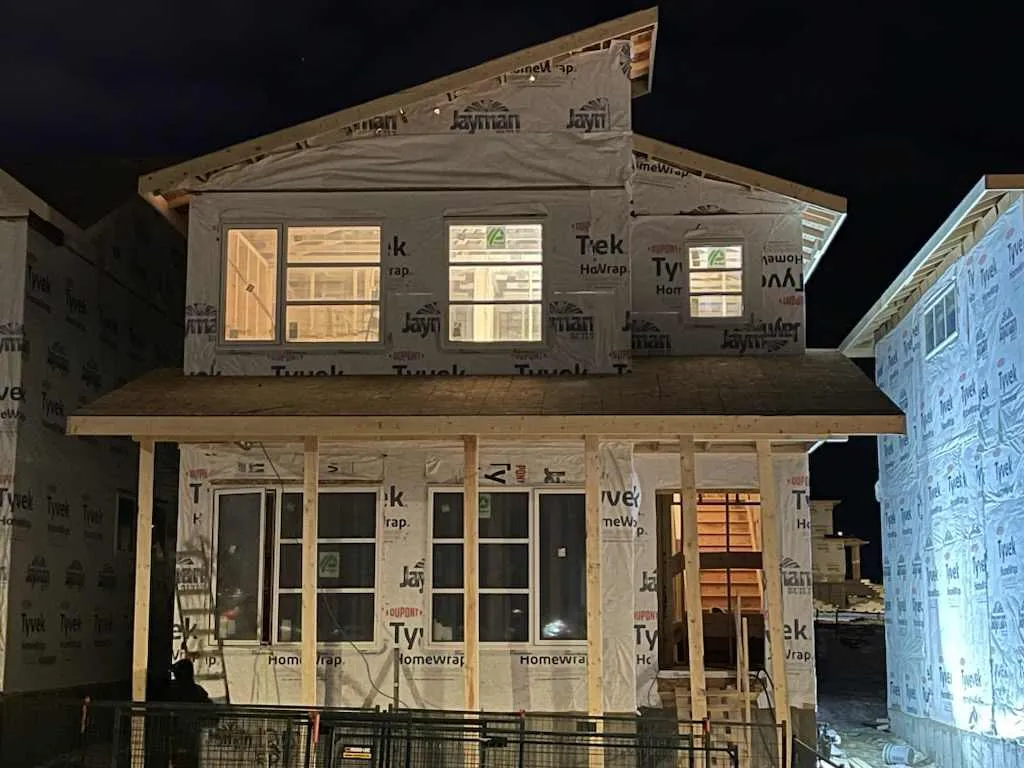 Framed single family home fully wrapped in house wrap, lit at night in Calgary