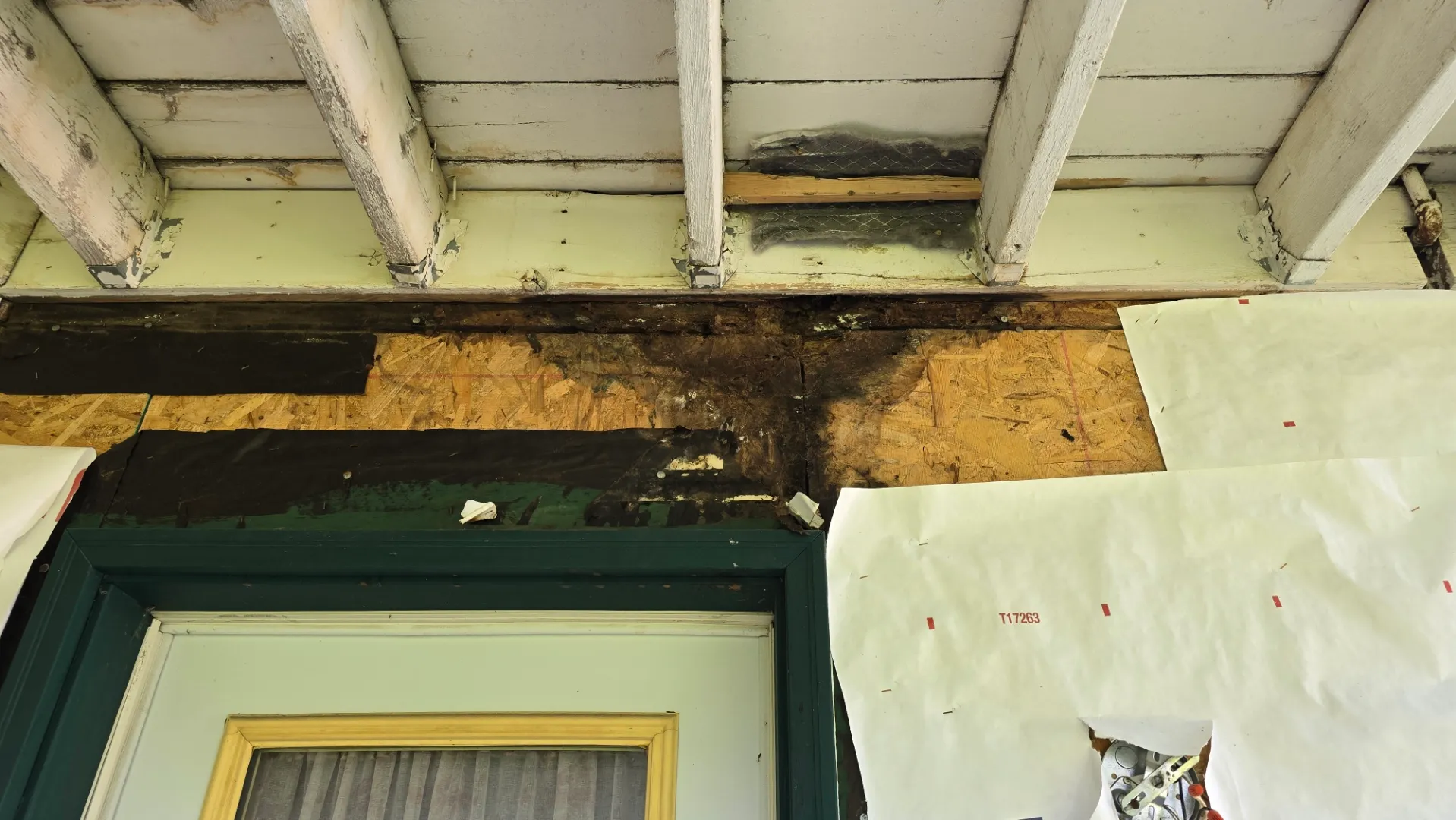 Water damage to a deck ledger board, wall sheathing and door jack studs, viewed from under the deck